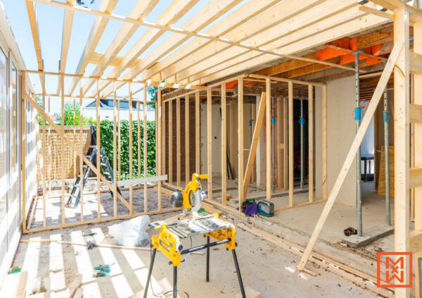 Huisverbouwing in volle gang: houten frame constructie met zaagtafel en gereedschap. Zicht op een open ruimte met blootliggende balken, klaar om te verbouwen en te bouwen.