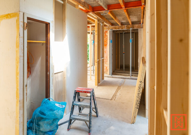 Binnenkant van een huis in renovatie. Houten frame constructie met gipsplaten, ladder, en blauwe afvalzak. Zicht op de renovatie van een interieur. DIY project in volle gang.