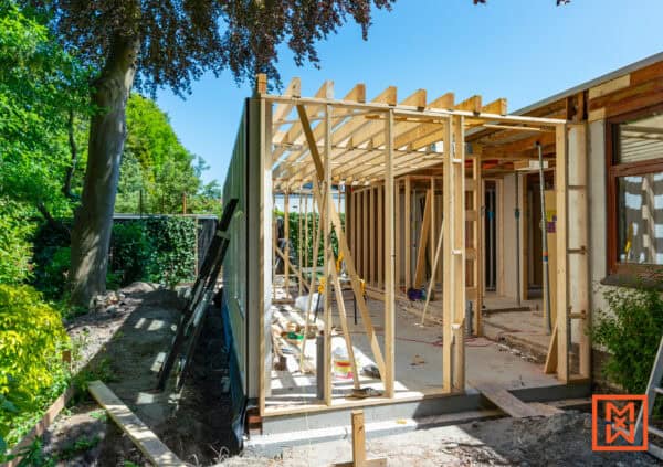 Houten frame van een huis uitbreiding in aanbouw, met zichtbare balken en steunbalken. Zonnige dag, bouwwerk in de tuin, klaar voor verdere verbouwing van het huis.