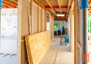 Interieur in aanbouw, met zicht op een gang in een huis tijdens een renovatie. Houten frames en multiplex platen liggen klaar voor de verbouwing. De renovatie van het huis is in volle gang.