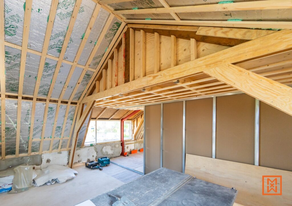 Zolder in aanbouw met houten constructie, isolatiemateriaal en gipsplaten. De ruwbouw van een zolderrenovatie, klaar voor isolatie en afwerking. Ideaal voor een verbouwing met extra leefruimte.