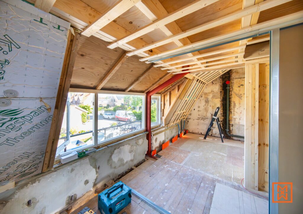 Zolder in renovatie met zicht op buiten. Houten constructie, dakisolatie en een blauwe Makita gereedschapskist op de vloer. Ideaal voor een zolderrenovatie.