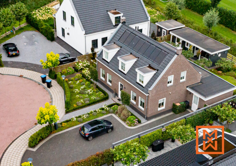 Luchtfoto van een charmant bakstenen huis met zonnepanelen, gelegen in een aangelegde buurt. Het huis beschikt over een goed onderhouden tuin en een verharde oprit met geparkeerde auto's. Een rustige, voorstedelijke omgeving is afgebeeld.