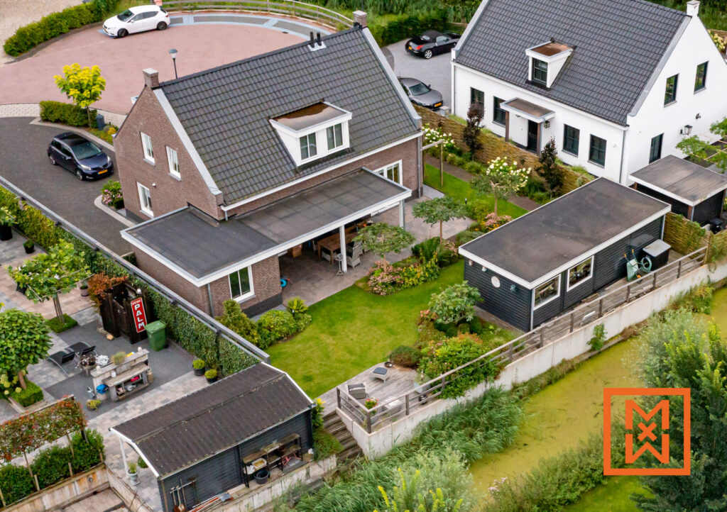 Luchtfoto van een charmante bakstenen woning met een ruime achtertuin, een moderne schuur en een weelderige tuin. De woning beschikt over een goed onderhouden gazon en terras, perfect om buiten te leven.