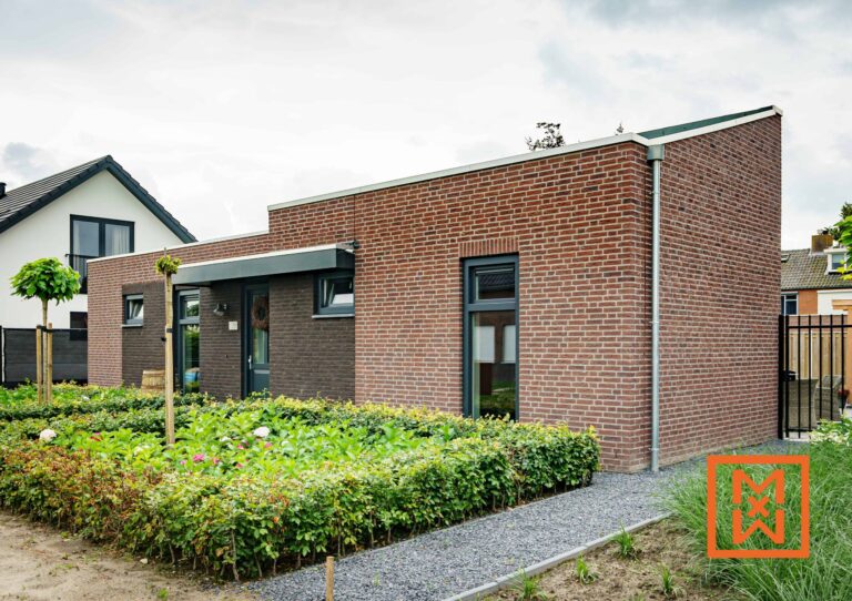 Moderne bakstenen woning met een strakke, donkergrijze deur en ramen, gelegen in een aangelegde tuin met een keurig gesnoeide haag en een grindpad. Het huis heeft een eigentijds ontwerp met een zadeldak. Nummer 14 is zichtbaar op het huis.