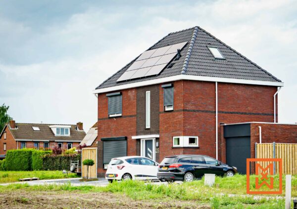 Moderne, twee verdiepingen tellende bakstenen woning met zonnepanelen op het dak, zwarte luiken aan de buitenkant en een ruime oprit met twee geparkeerde auto's. De woning ligt in een rustige woonwijk en is een toonbeeld van eigentijds woningontwerp en duurzame energieoplossingen.