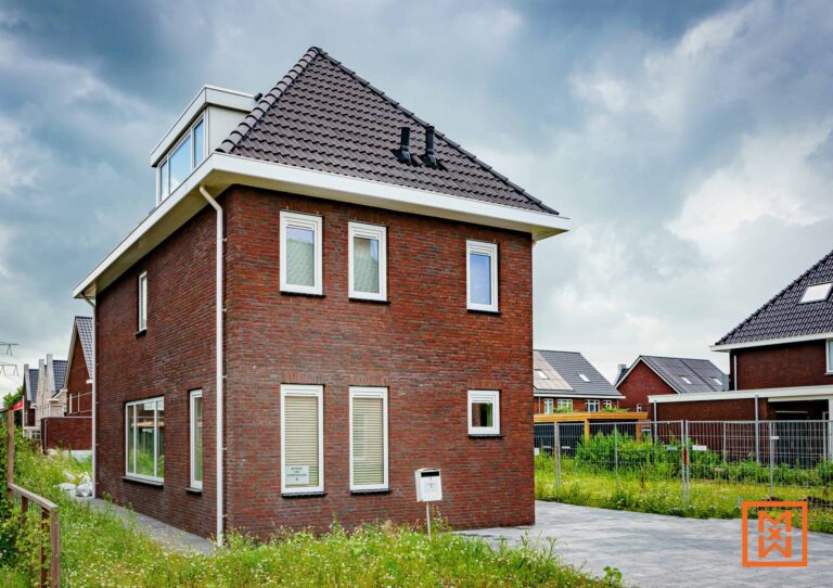 Nieuwe bakstenen woning met dakkapel, witte kozijnen en beige jaloezieën. Het huis staat op een grasveld met een verhard pad en maakt deel uit van een nieuwbouwwijk. Een brievenbus met het adreslabel "Reynder van Hermetenlaan 5" is zichtbaar.