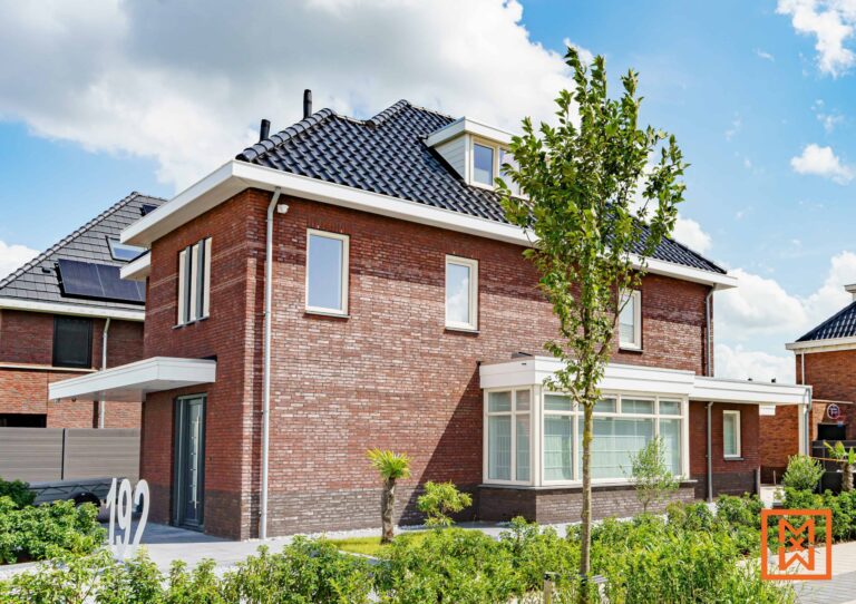Modern huis van rode baksteen met witte afwerking, nummer 192 prominent aanwezig. Het huis heeft een eigentijds ontwerp met grote ramen en een keurig aangelegde voortuin. Naast het huis staat een boom onder een strakblauwe lucht.