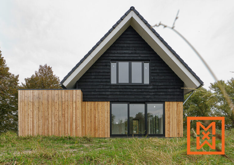 Moderne A-frame woning in zwart en licht hout, gelegen in een grasveld. De woning heeft grote ramen en een strak design.