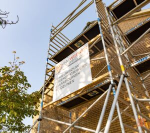 Aluminium steigers staan fier tegen een bakstenen gebouw dat gerenoveerd wordt. Een groot bord van Van Weenen Bouwbedrijf adverteert met nieuwbouw, renovatie en raaminstallatie.
