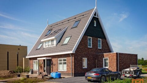 Nieuw bakstenen huis met een steil dak, zonnepanelen en een auto op de oprit. door Van Weenen Bouwbedrijf