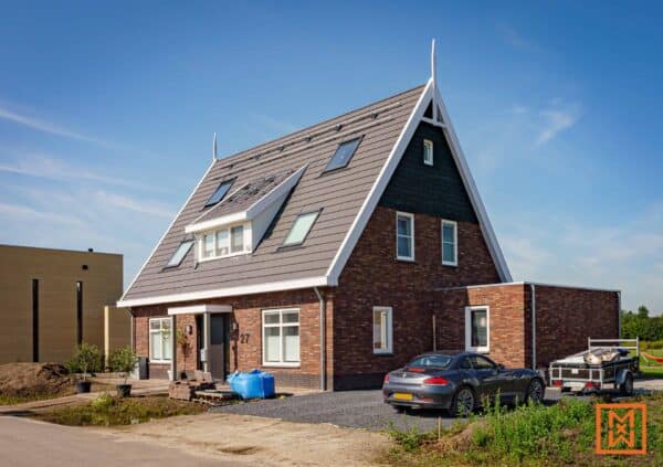 Nieuw bakstenen huis met een steil dak, zonnepanelen en een auto op de oprit. door Van Weenen Bouwbedrijf