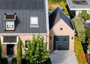 Woningen met donkere dakpannen en bakstenen muren, omgeven door groene bomen en heggen. Een moderne, rustige woonwijk.