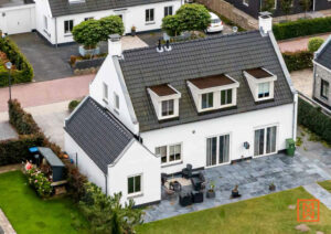 Wit huis met donker dak en dakkapellen, omgeven door een groene tuin met terras en tuinset. Een sfeervol familiehuis in een rustige woonwijk.