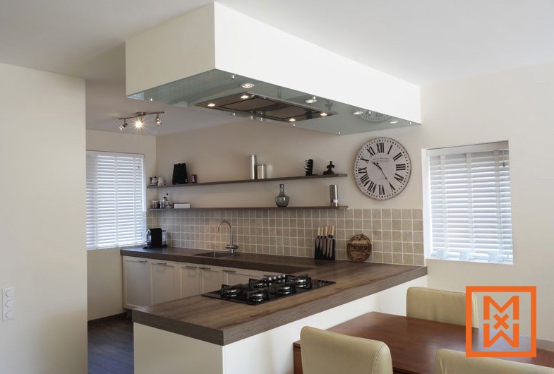 Moderne keuken met strakke witte kasten, een donkerhouten kookeiland en een afzuigkap met glazen afdekplaat. Een beige tegelachterwand en zwevende planken dragen bij aan het eigentijdse design. Witte jaloezieën en een grote klok maken het plaatje compleet.