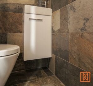 Modern bathroom with dark stone tiles and white vanity unit. Afbouw en inrichting woning. door Van Weenen Bouwbedrijf