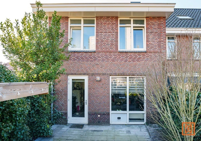 Bakstenen huis met ramen en deur, omgeven door groen. Achtertuin met bestrating.