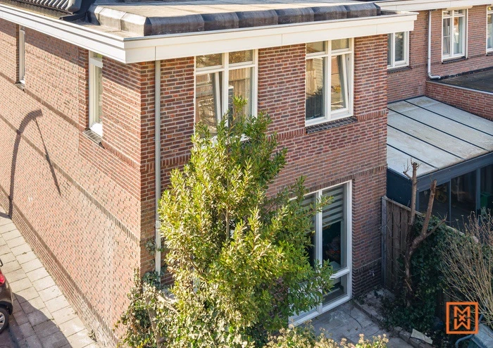 Bakstenen huis met witte kozijnen en groene boom in de tuin. Modern woonhuis met plat dak.