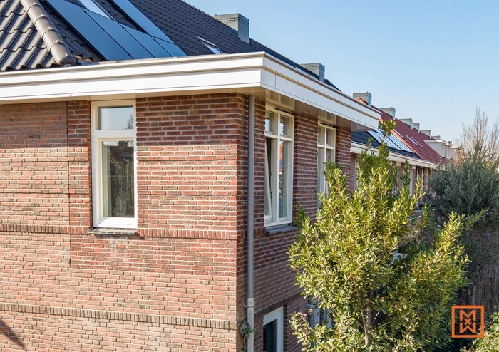 Bakstenen huis met witte kozijnen en dakpannen met zonnepanelen in een woonwijk.