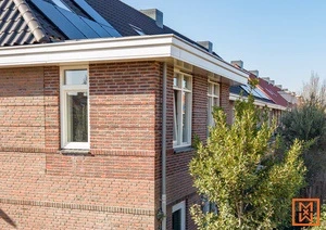 Bakstenen huis met witte kozijnen en zonnepanelen op het dak in een woonwijk.