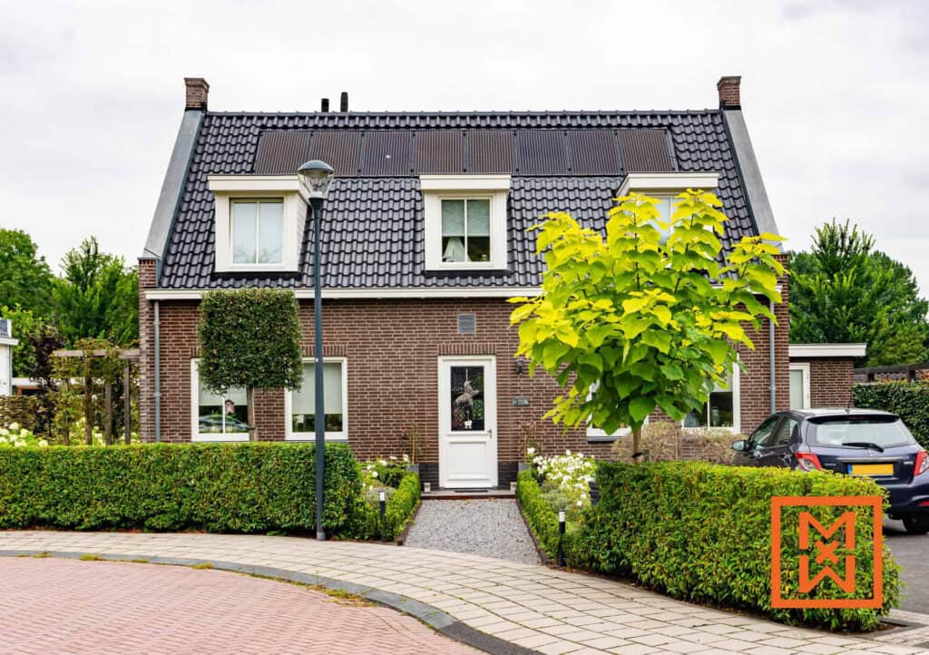 Bungalow met zonnepanelen en groene tuin, naast een auto.
