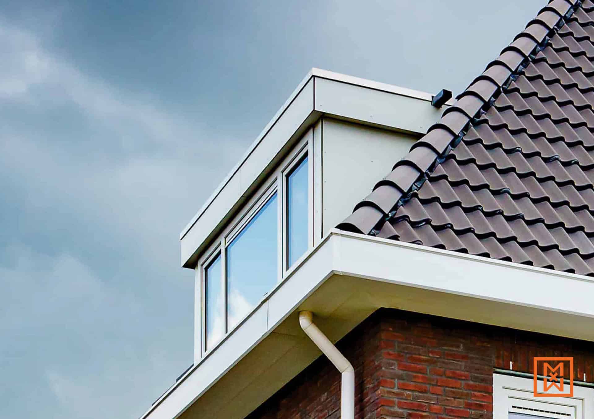 Detail van een huis met een dakraam, bruine dakpannen, witte dakranden en een rode bakstenen muur tegen een bewolkte lucht.