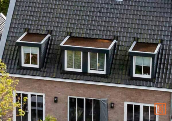 Dakraam met drie dakkapellen op een donker dak van een bakstenen huis. Witte ramen contrasteren met de donkere dakpannen.