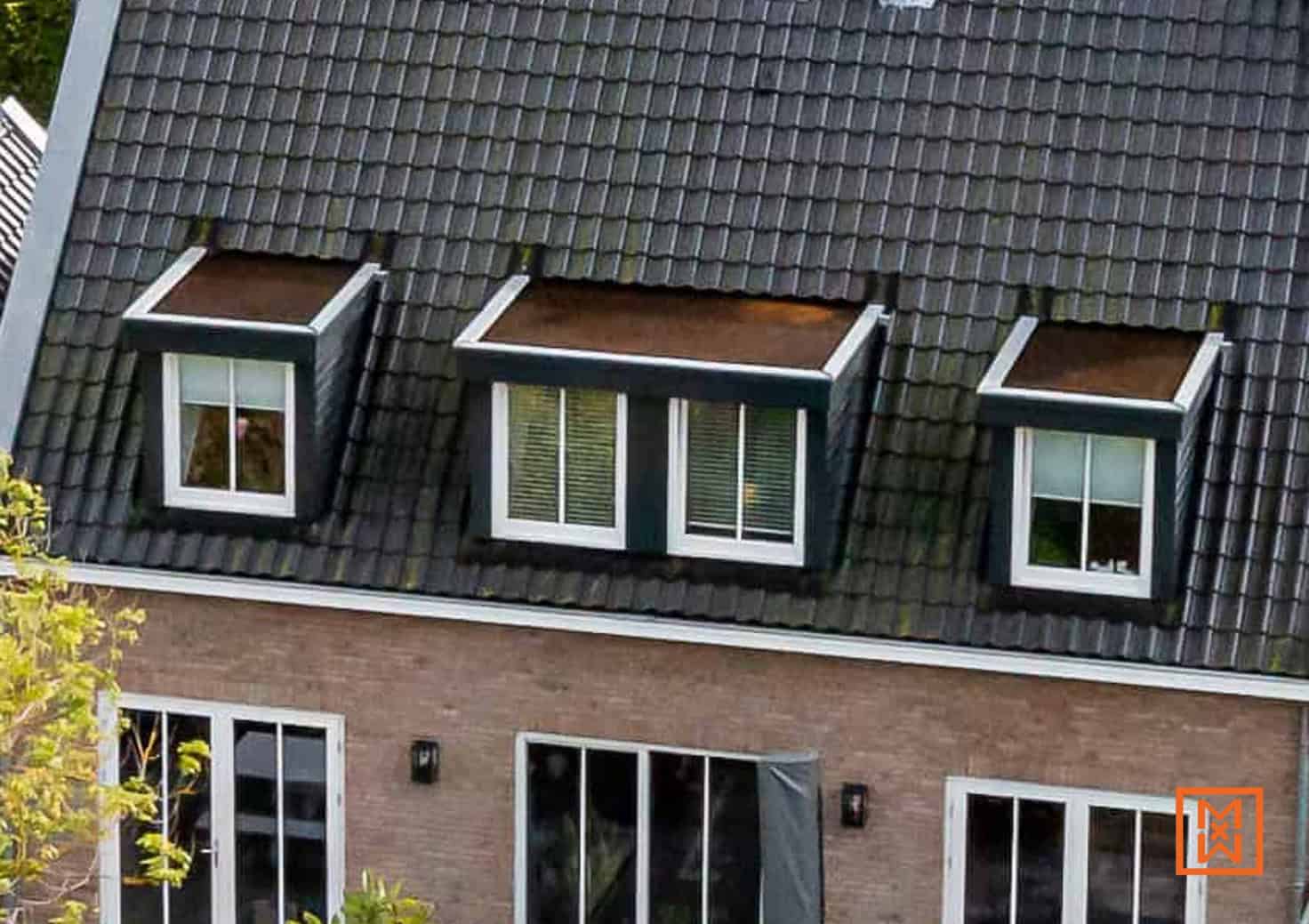 Dakraam met drie dakkapellen op een donker dak van een bakstenen huis. Witte ramen contrasteren met de donkere dakpannen.