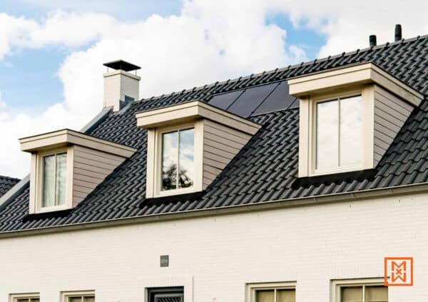 Drie dakkapellen met witte kozijnen op een dak met zwarte dakpannen. Zonnepanelen zijn discreet geïntegreerd. De gevel is wit geschilderd. Modern en energiezuinig design.