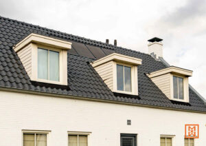 Witte bakstenen huis met donker dak en drie dakkapellen. Zonnepanelen subtiel geïntegreerd in het dak. Een klassieke en moderne uitstraling.