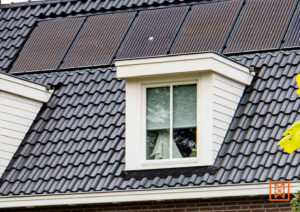Een dak met zwarte dakpannen en zonnepanelen, met een dakkapel met witte omlijsting. Een huis met duurzame energieoplossingen.