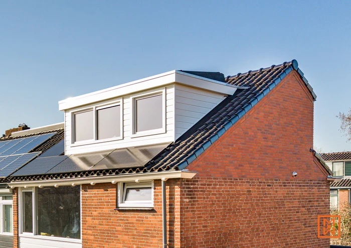 Dakkapel op een bakstenen huis met dakpannen en zonnepanelen in Nederland.