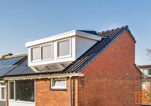 Dakkapel op bakstenen huis met zonnepanelen onder een heldere blauwe hemel.