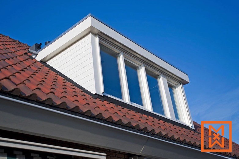 Dakkapel met vier witte ruiten, die licht en architectonische accenten toevoegen aan een rood pannendak. De dakkapel is bekleed met witte gevelbekleding en steekt af tegen een helderblauwe lucht.
