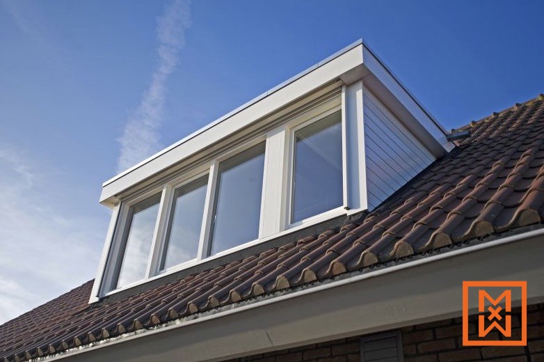 Moderne dakkapel met wit kozijn en drie grote ruiten, geplaatst op een bruin pannendak tegen een helderblauwe lucht. De dakkapel zorgt voor extra ruimte en licht in huis.