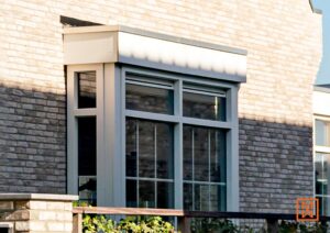 Moderne grijze raamkozijnen in een bakstenen muur. Het raam heeft een strak ontwerp met meerdere ruiten. De bakstenen variëren in kleur, van lichtbeige tot donkergrijs.