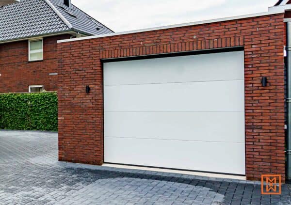 Moderne witte garagedeur in een rode bakstenen garage. Strak design, grijze bestrating.