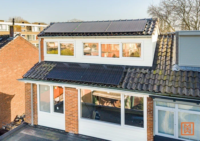 Huis met zonnepanelen op het dak en dakkapel met ramen, bakstenen en witte gevelbekleding.