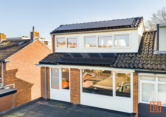 Huis met zonnepanelen op het dak en dakkapel, bakstenen en witte gevelbekleding.
