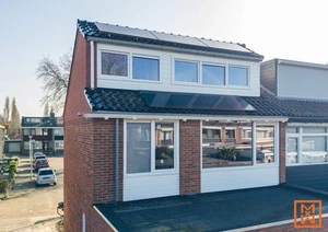 Huis met zonnepanelen op de uitbouw. Bakstenen en witte kozijnen. Zonnige dag.