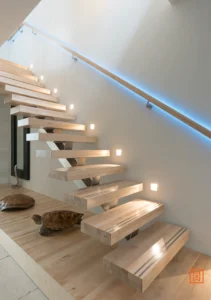 Moderne, zwevende houten trap met minimalistisch design en subtiele verlichting. Twee decoratieve schildpadden sieren de basis van de trap. Strakke lijnen en warme houttinten creëren een stijlvolle sfeer.