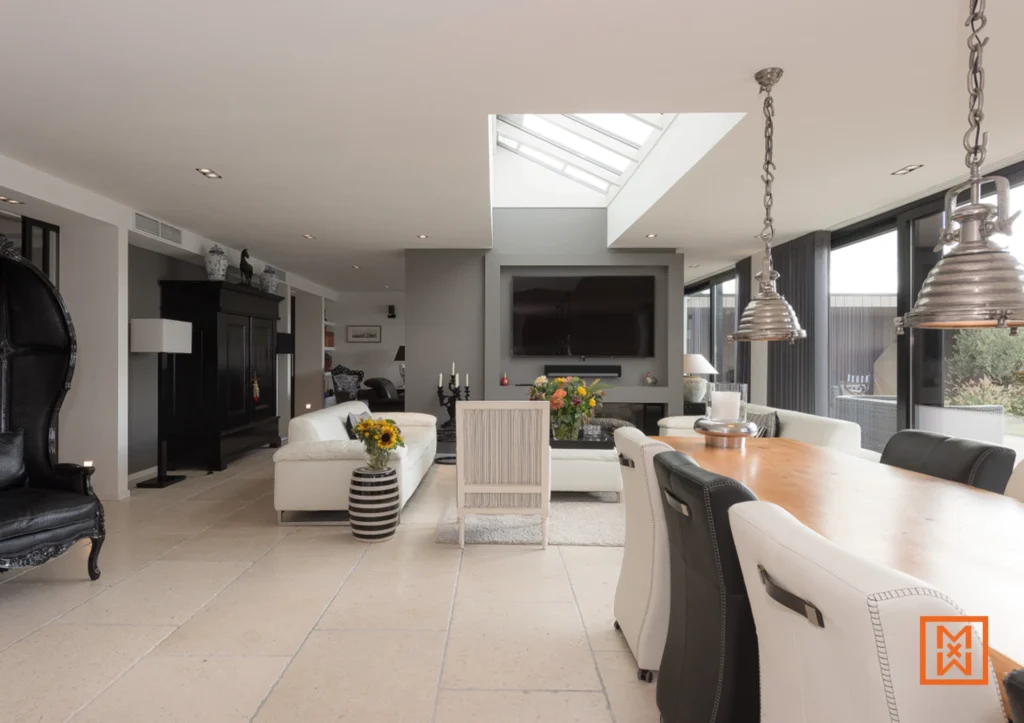 Ruime woonkamer met luxe inrichting: witte bank, zwarte kast, design lampen en grote ramen met uitzicht op de tuin. Stijlvol interieur met veel lichtinval.