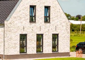 Een modern huis met witte bakstenen en zwarte raamkozijnen. De architectuur combineert strakke lijnen met een landelijke uitstraling.