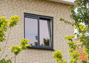 Een modern draai-kiepraam met een donkergrijs kozijn in een gevel van gele baksteen. De bakstenen zijn in een decoratief patroon rond het raam geplaatst.