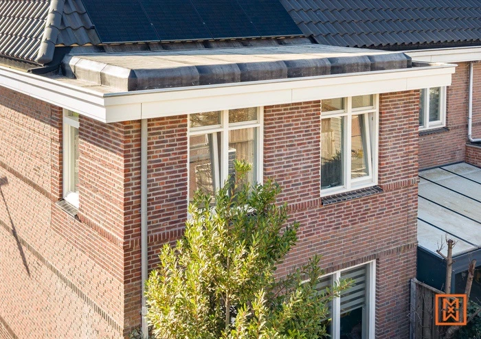 Modern huis met plat dak, bakstenen gevel en witte kozijnen. Zonnepanelen op het dak.