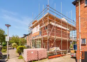 Nieuwbouw huis in aanbouw met steigers en rode bakstenen onder blauwe lucht.