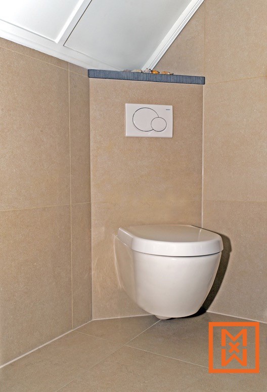 Modern wandcloset in een hoek, met een beige betegelde badkamer en een toiletreservoir met dubbele spoeling. Het strakke, minimalistische ontwerp creëert een serene sfeer.