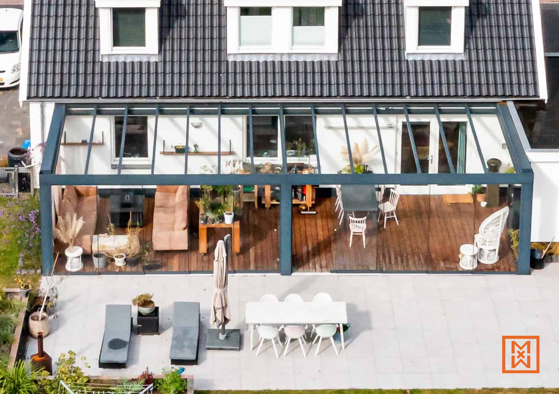 Een serre met een modern design, uitgerust met comfortabele meubels en een houten vloer, die een naadloze overgang biedt naar een betegeld terras met een eethoek en ligstoelen.