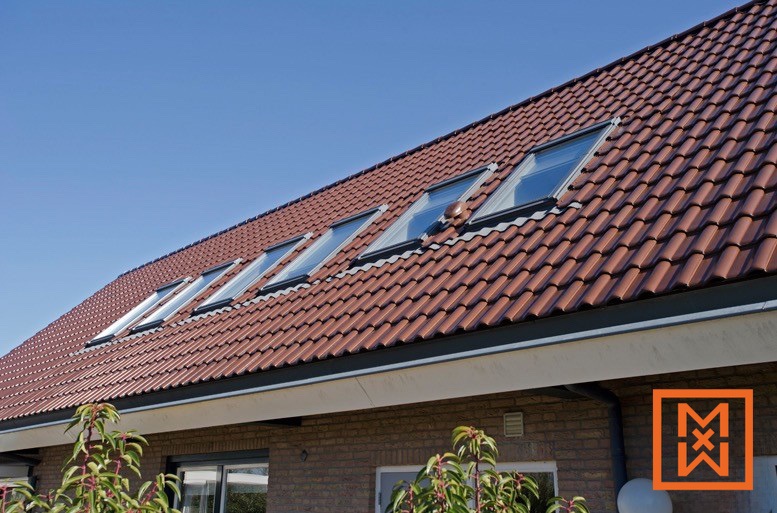 Een rij moderne dakramen is naadloos geïntegreerd in een terracotta dakpan, waardoor er natuurlijk licht in de woning valt. De daklijn loopt geleidelijk af tegen een helderblauwe lucht.