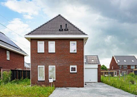 Modern bakstenen huis met grijze dakpannen en witte kozijnen. Strakke architectuur in een nieuwe woonwijk met veel groen. Zonnepanelen zichtbaar op de garage.
